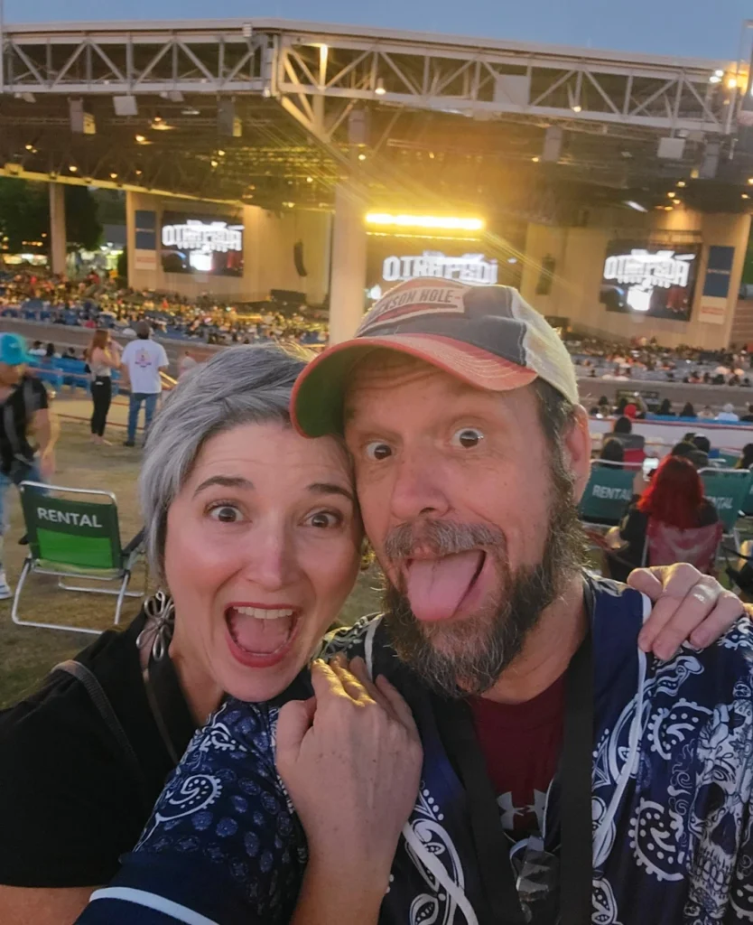 About A couple smiles excitedly in front of an outdoor concert stage