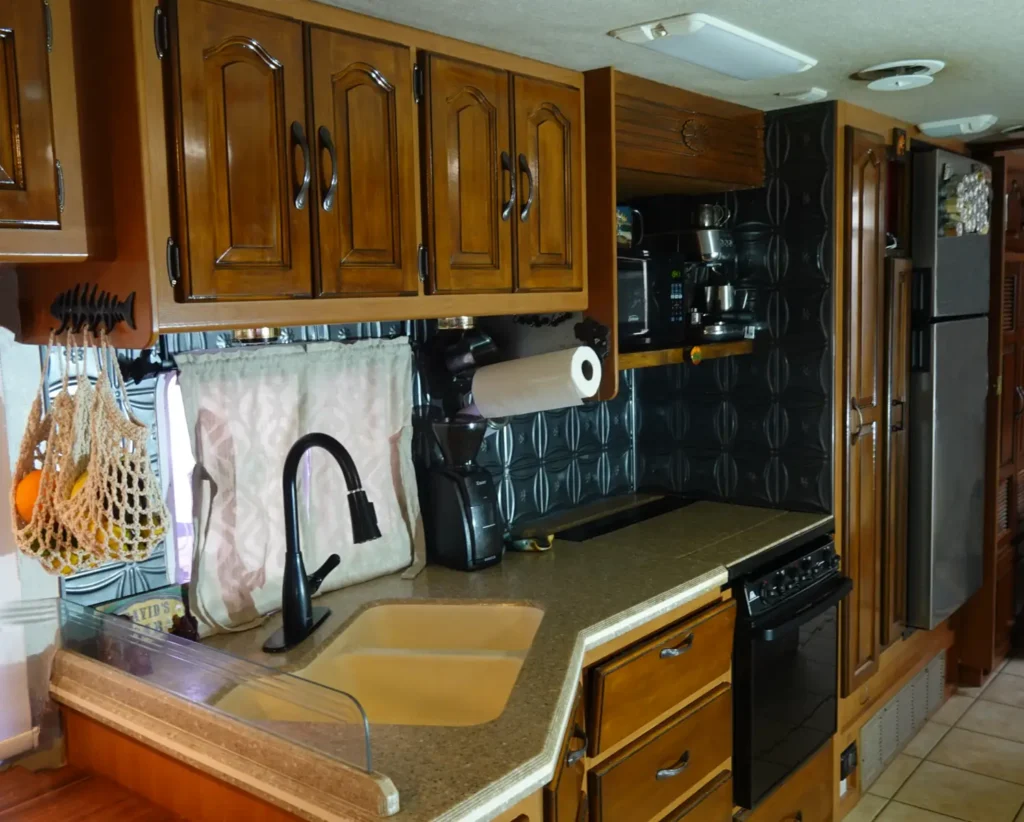 A close up of a small RV kitchen with fruit hammock in the forefront, magnetic paper towel holder coffee bar and refrigerator spice rack visible to the rear