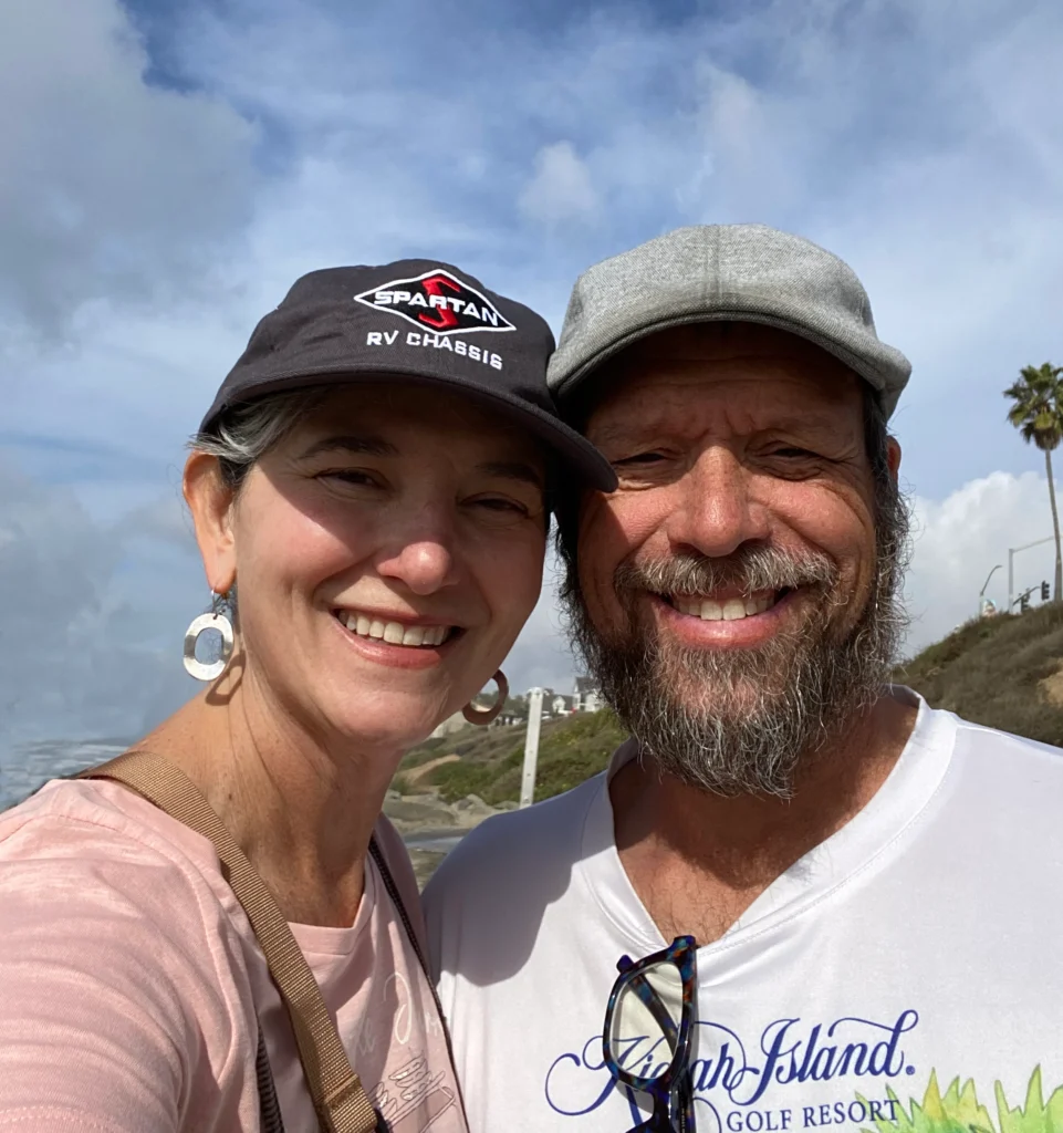 A couple smiles at the cameral on a bright sunny day with blue skies behind them