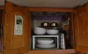 an open kitchen cabinet with plates and bowls stacked on a shelf insert and wine glasses hanging from a glass rack