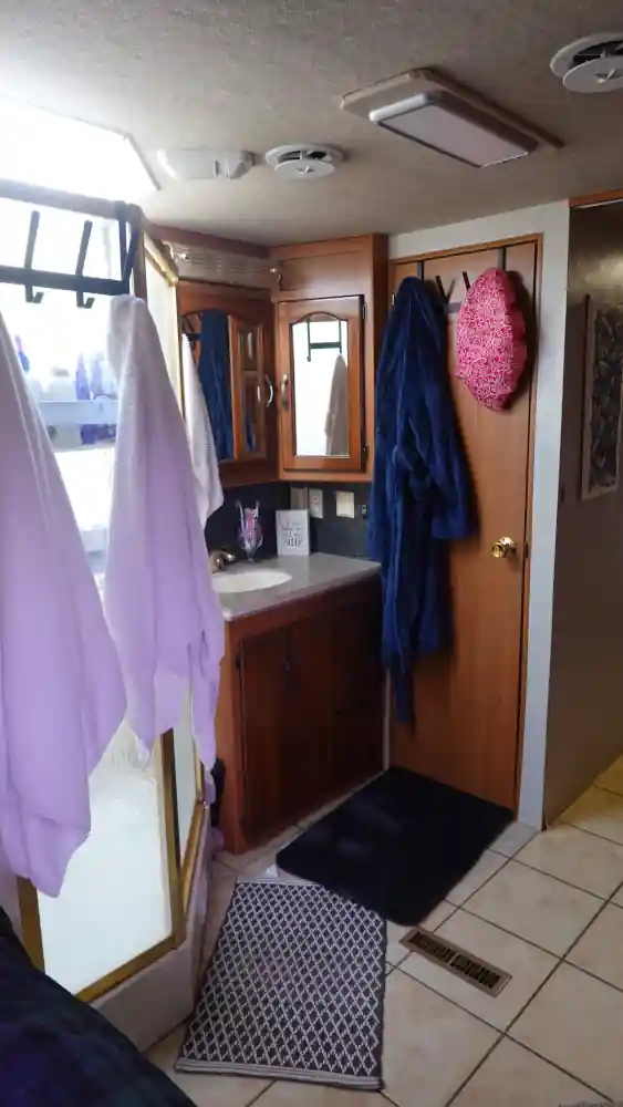 A small RV bathroom is in view featuring over the door hangers for towels and robes