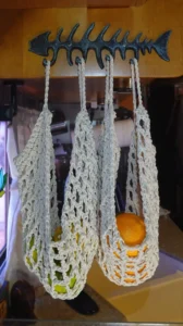 a cream colored crotched bag holding oranges, lemons and limes hangs from a decorative metal fish skeleton