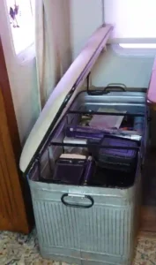 a padded metal storage bench sits open with blender and other kitchen items visible