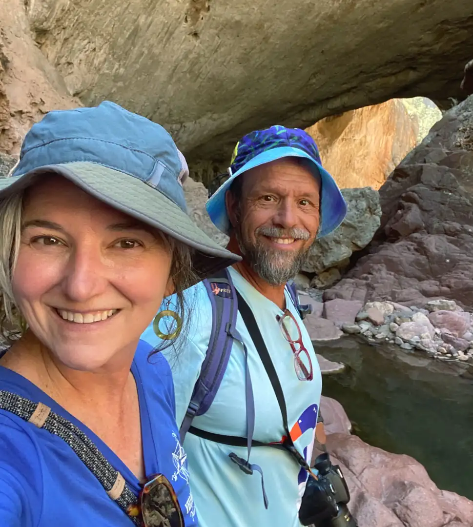 A couple dressed in blue hiking gear smile in front of a rock formation