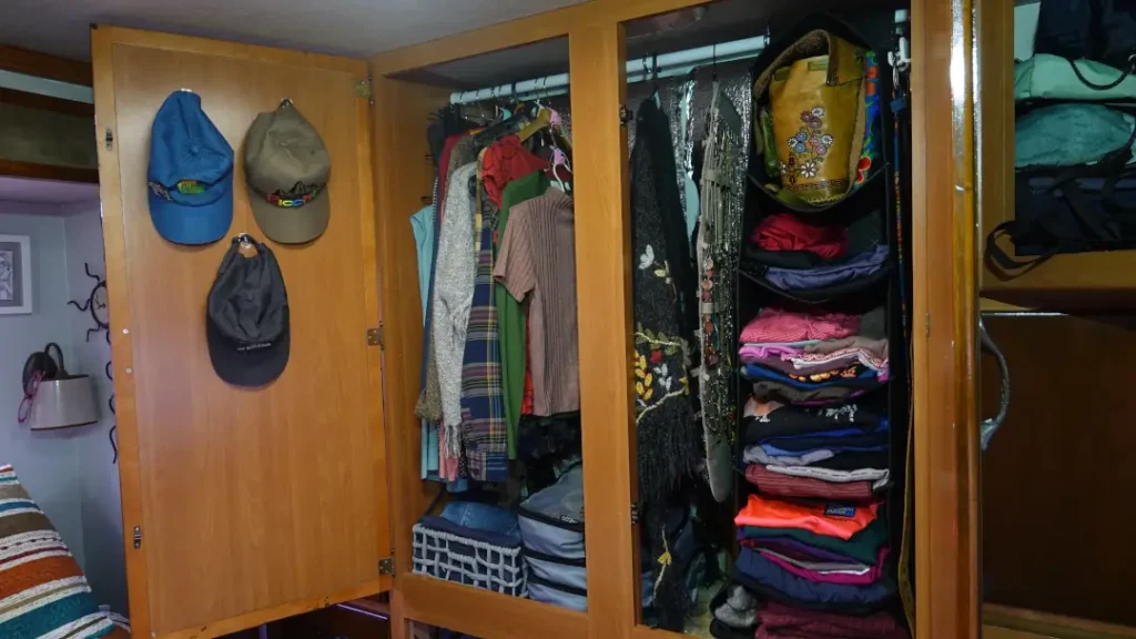 An RV wardrobe stands open showcasing hanging shelves, a jewelry holder, packing cubes, baskets, cascading hangs and hooks used to organize the space