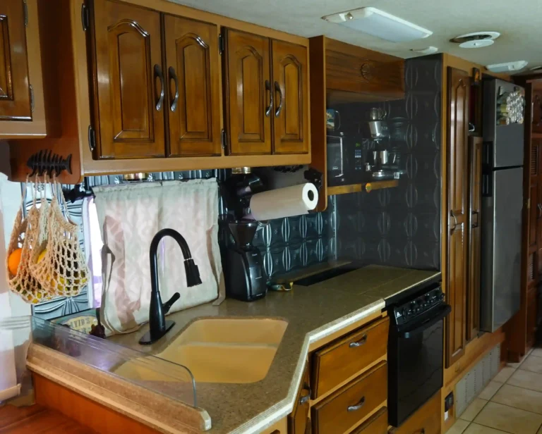 A close up of a small RV kitchen with fruit hammock in the forefront, magnetic paper towel holder coffee bar and refrigerator spice rack visible to the rear