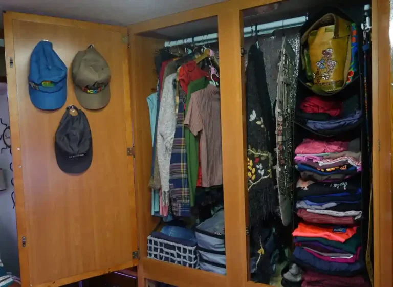 An RV wardrobe stands open showcasing hanging shelves, a jewelry holder, packing cubes, baskets, cascading hangs and hooks used to organize the space
