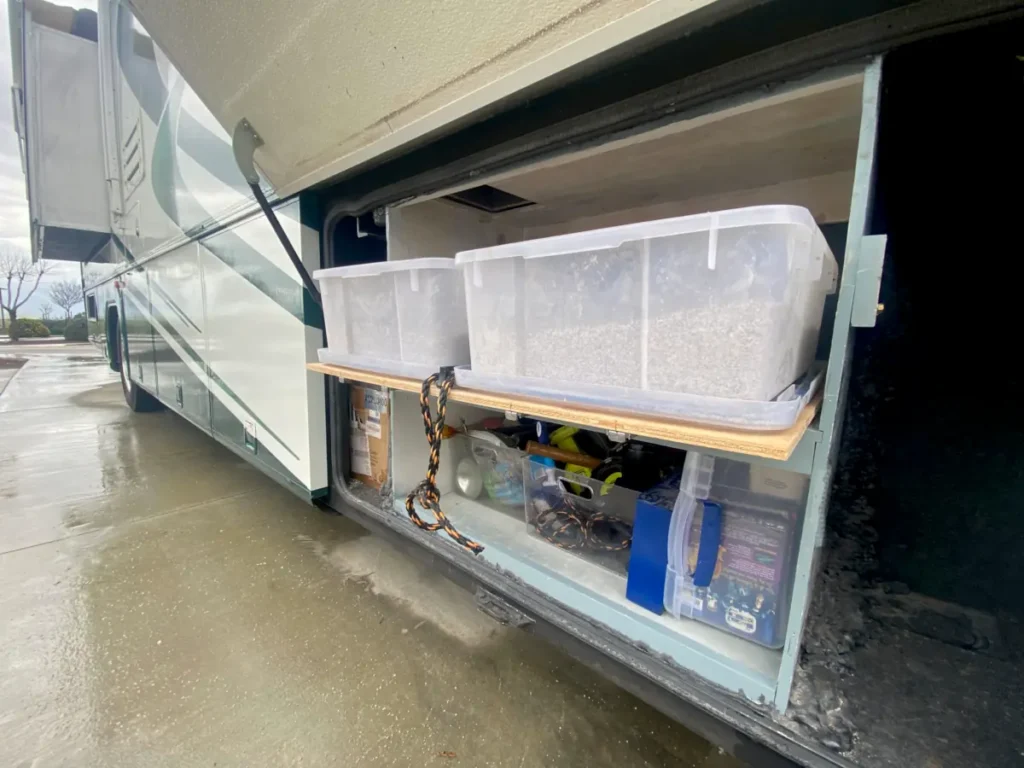 An open rv bay reveals an open sided box with a litter box tray on the top shelf with access hole visible in the upper left corner