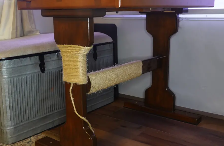 The leg and cross brace of a kitchen table is wrapped in sisal rope creating a cat scratching place