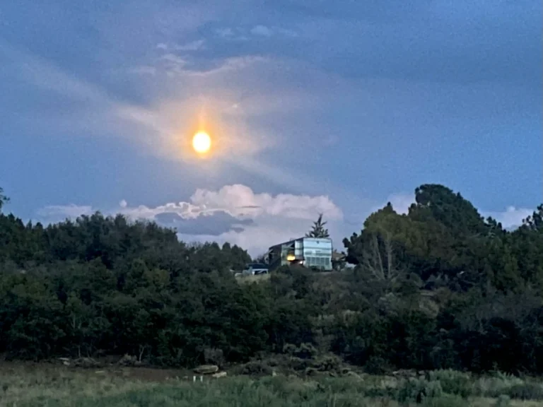 A motorhome is parked on the edge of a small hill lit by a full moon.